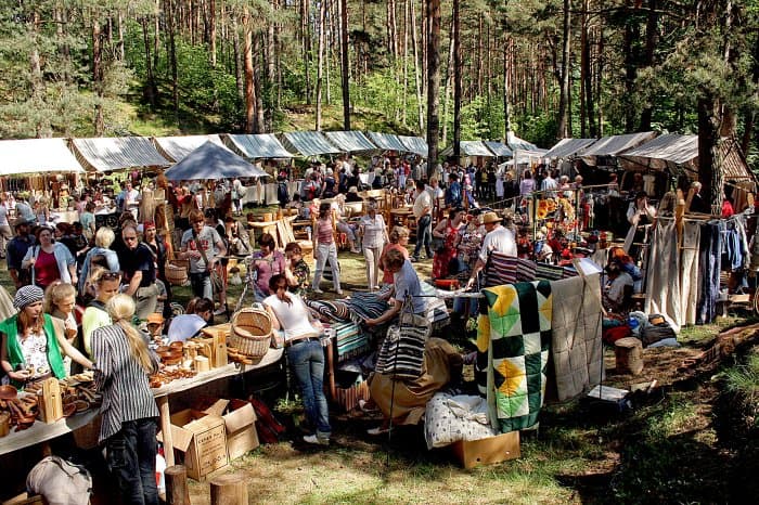 Vibrant outdoor market with vendors and shoppers in a forest setting.