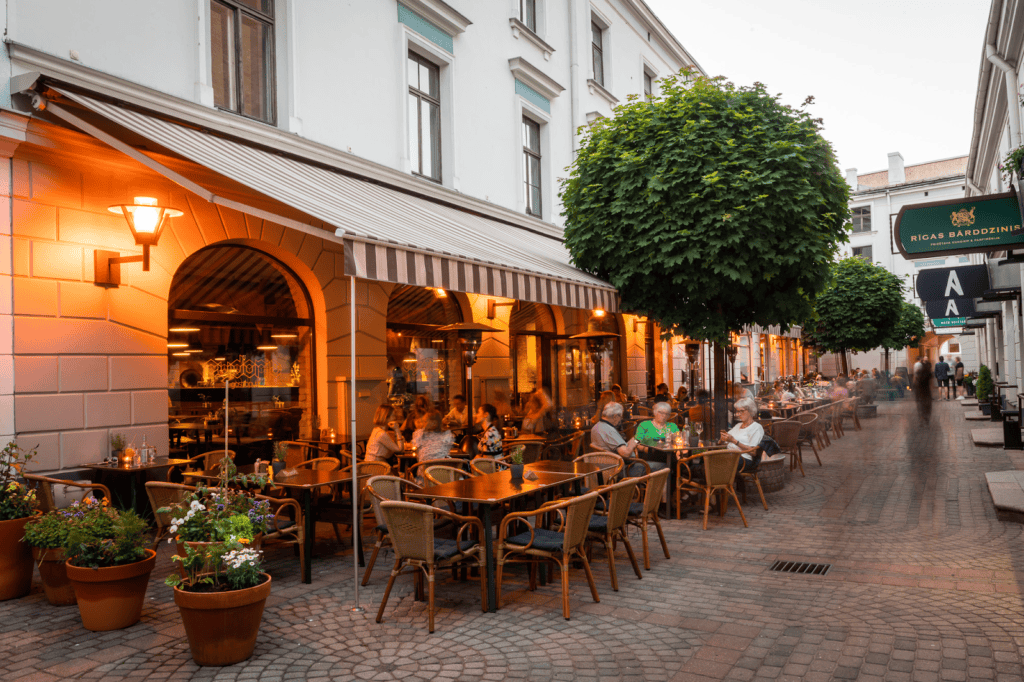 Vakarā ārpusē esoša restorāna terase ar apmeklētājiem, Rīgas centrā.