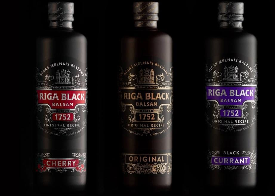 Three Riga Black Balsam bottles with cherry, original, and currant flavours on a dark background.